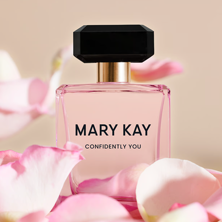 Mary Kay Confidently You Parf&uuml;mflakon, umgeben von rosa Bl&uuml;tenbl&auml;ttern vor einem weichgezeichneten Hintergrund.